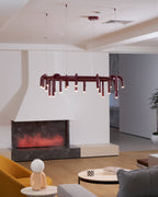 Red Clérachic ring chandelier seen from slightly below, in front of a white fireplace, with an ochre chair in the corner.