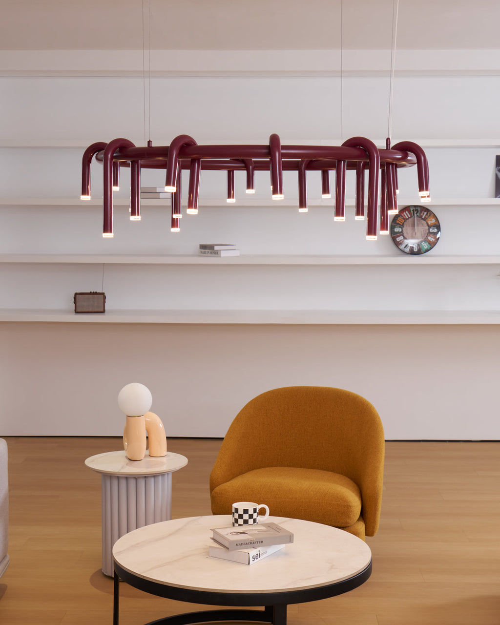 Ring chandelier in red from Clérachic, with a dense set of downward heads, hung in front of white wall shelves and an ochre chair.