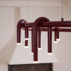Close view of the arched red tubes of this Clérachic chandelier, each ending in a frosted light cap beneath the ring.