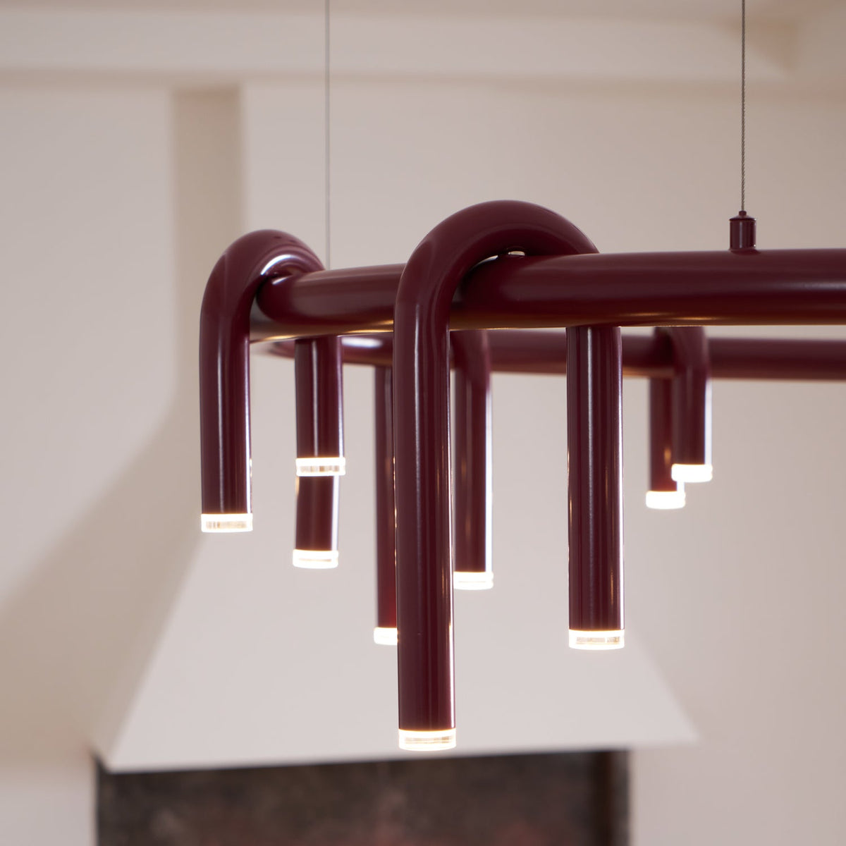 Close view of the arched red tubes of this Clérachic chandelier, each ending in a frosted light cap beneath the ring.