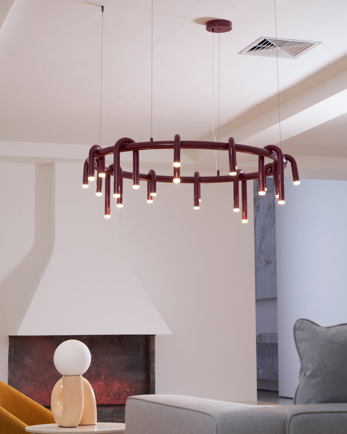 Red Clérachic ring chandelier in front of a white fireplace hood, hung from a round red canopy on a ceiling with a vent.