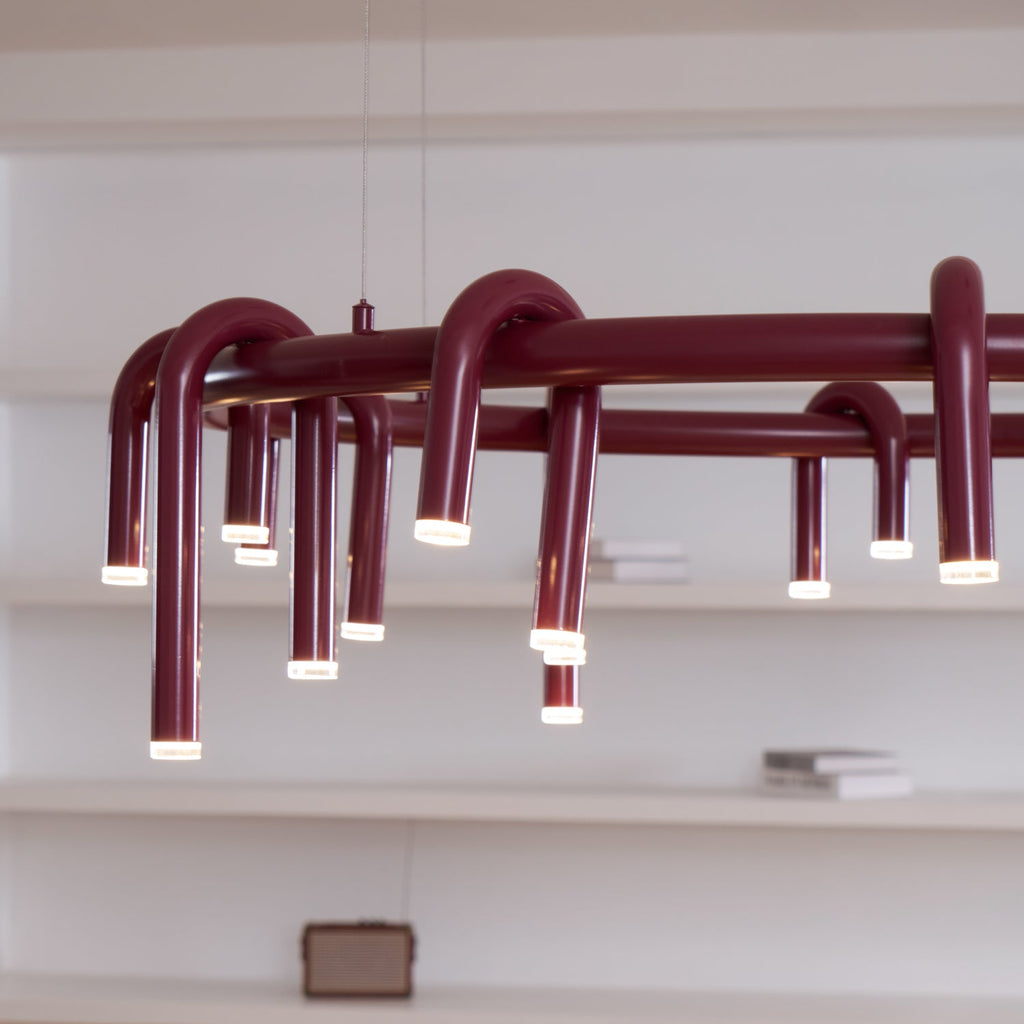 Close angled view of the red ring and its looping tubes on this Clérachic chandelier, with white shelves behind.