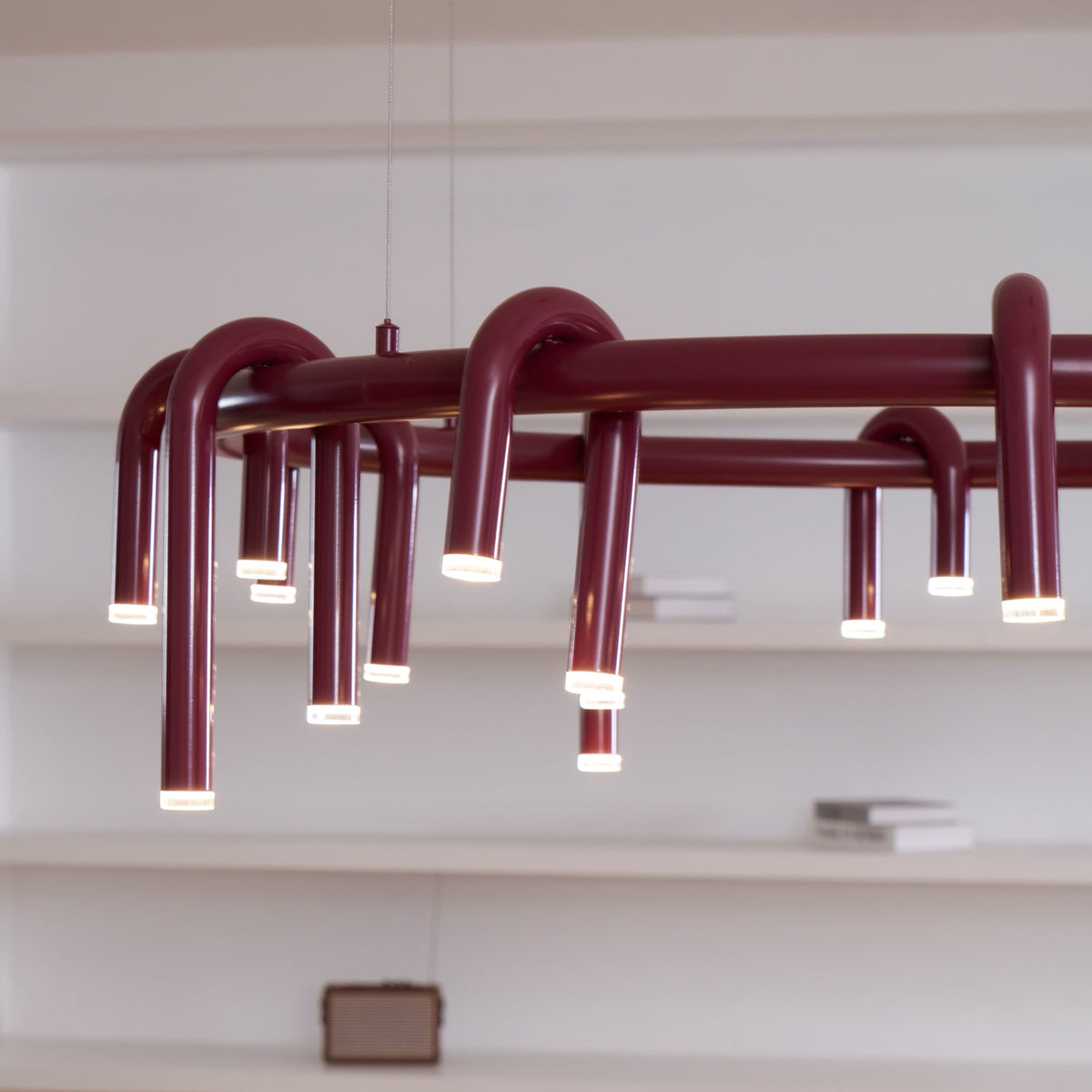 Close angled view of the red ring and its looping tubes on this Clérachic chandelier, with white shelves behind.