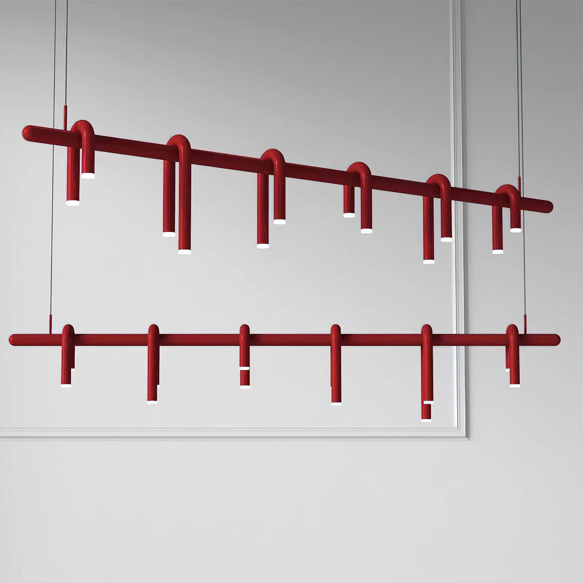 Two views of the linear red chandelier from Clérachic, one tilted and one straight, against a pale grey wall.