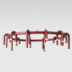 Red Clérachic ring chandelier photographed in front of a pale grey backdrop, with thin wires and arched tubes around the frame.
