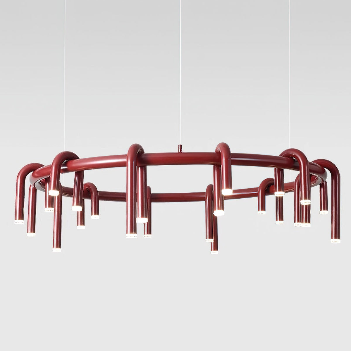 Red Clérachic ring chandelier photographed in front of a pale grey backdrop, with thin wires and arched tubes around the frame.