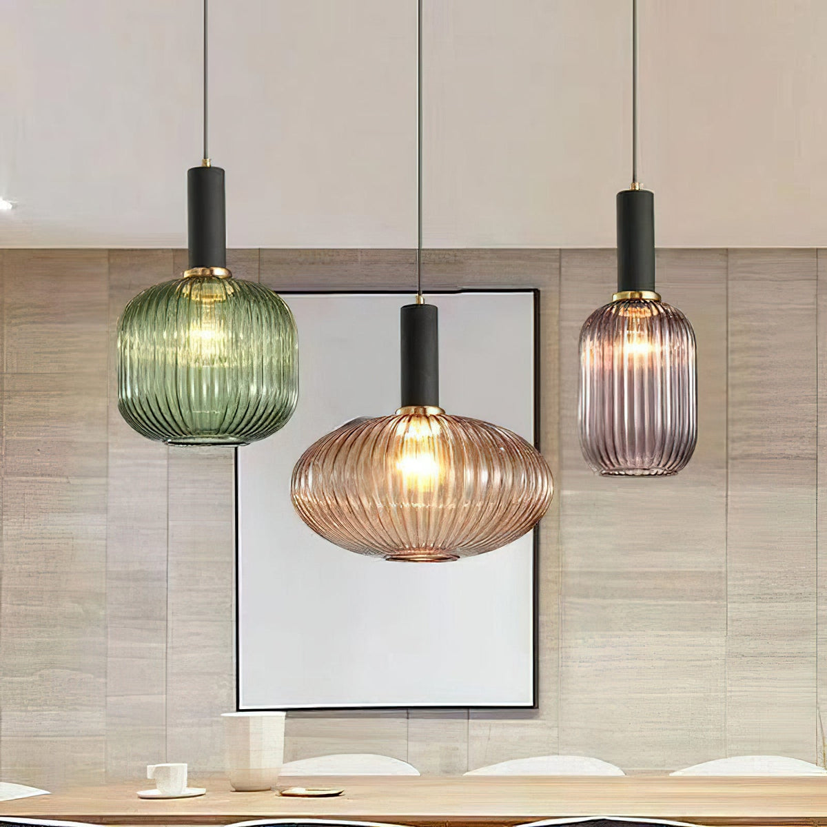 Green, amber and smoke grey reeded glass shades from Clérachic hang with black fittings over a wooden dining table and a framed picture.