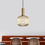 This Clérachic pendant has a small rounded amber glass shade and gold fitting, hung against a pale grey wall above a rust-coloured banquette.