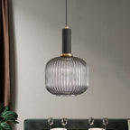 A rounded smoke grey reeded glass shade from Clérachic with a black fitting, hanging against a grey wall above a set dining table.