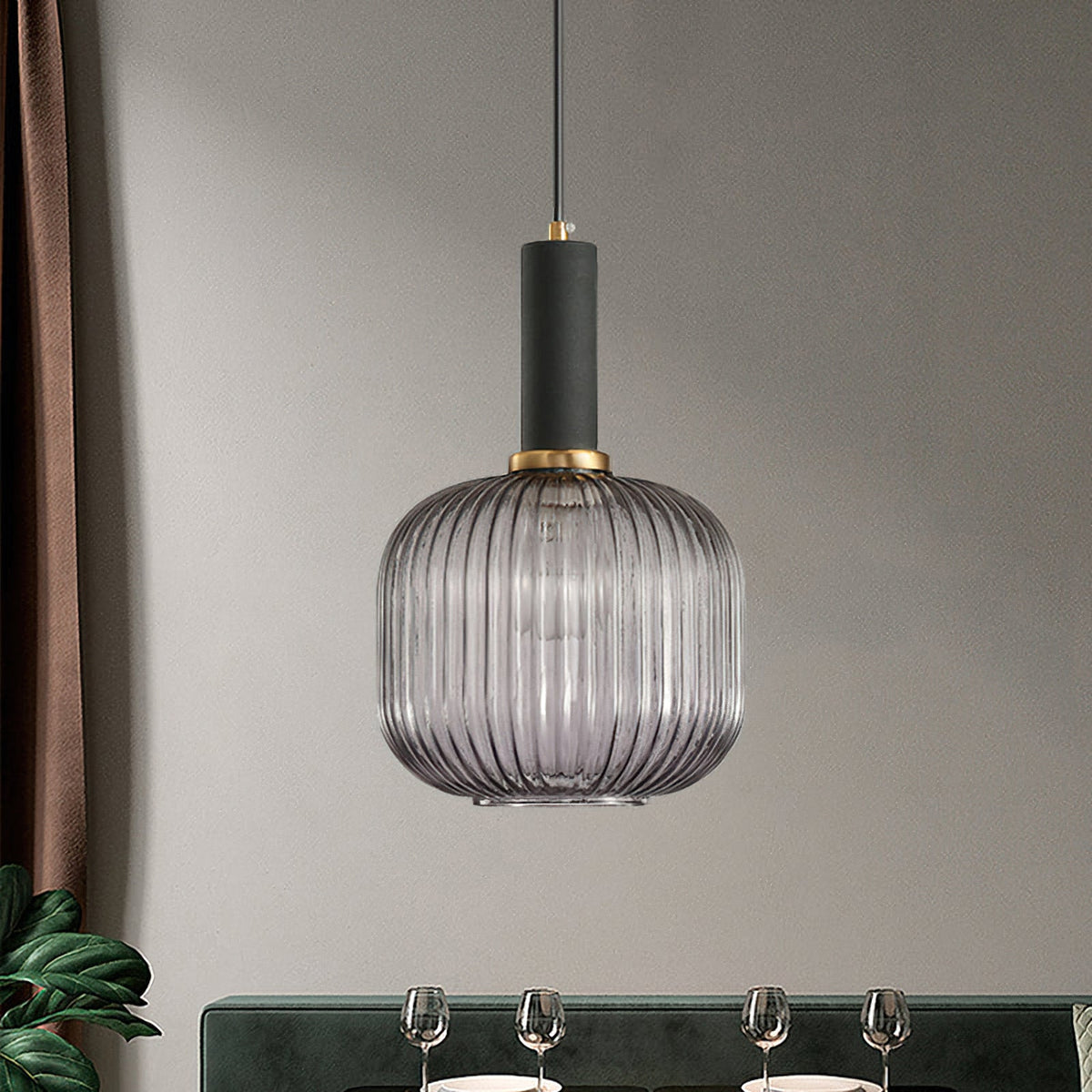 A rounded smoke grey reeded glass shade from Clérachic with a black fitting, hanging against a grey wall above a set dining table.