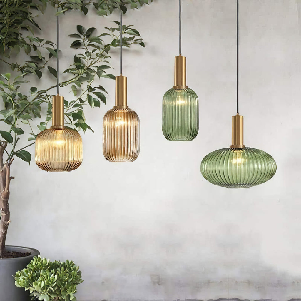 Four Clérachic reeded glass pendants in amber and green, in tall and flat shapes, hang at staggered heights beside a leafy indoor plant.