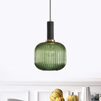 Round green reeded glass shade on a black fitting with a gold ring, from Clérachic, hanging against white with a bowl of yellow squash below.