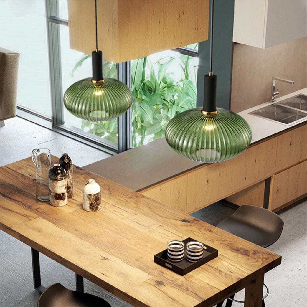 From above, two green reeded glass pendants from Clérachic hang with black fittings over a wooden kitchen island with a window behind.
