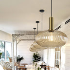Large flat amber reeded glass pendant from Clérachic on a gold stem, with two more behind it, in a bright room with white-painted beams.