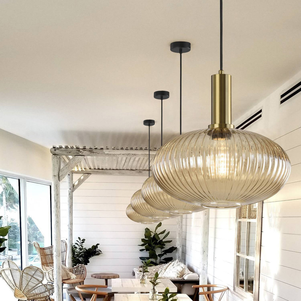 Large flat amber reeded glass pendant from Clérachic on a gold stem, with two more behind it, in a bright room with white-painted beams.