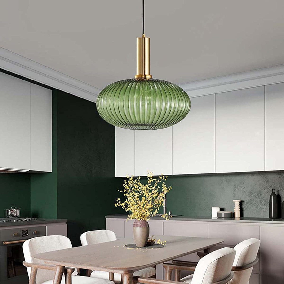 A flat green reeded glass pendant from Clérachic on a gold stem hangs in a kitchen with dark green walls, white cabinets and a wooden table.