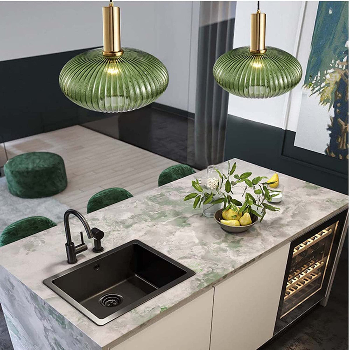 Two flat green reeded glass pendants from Clérachic with gold stems, lit, hang over a marbled kitchen island with a black sink.