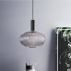 Smoke grey reeded glass pendant from Clérachic with a black fitting, hanging against a blue-grey wall beside a poster and a desk pot of pencils.