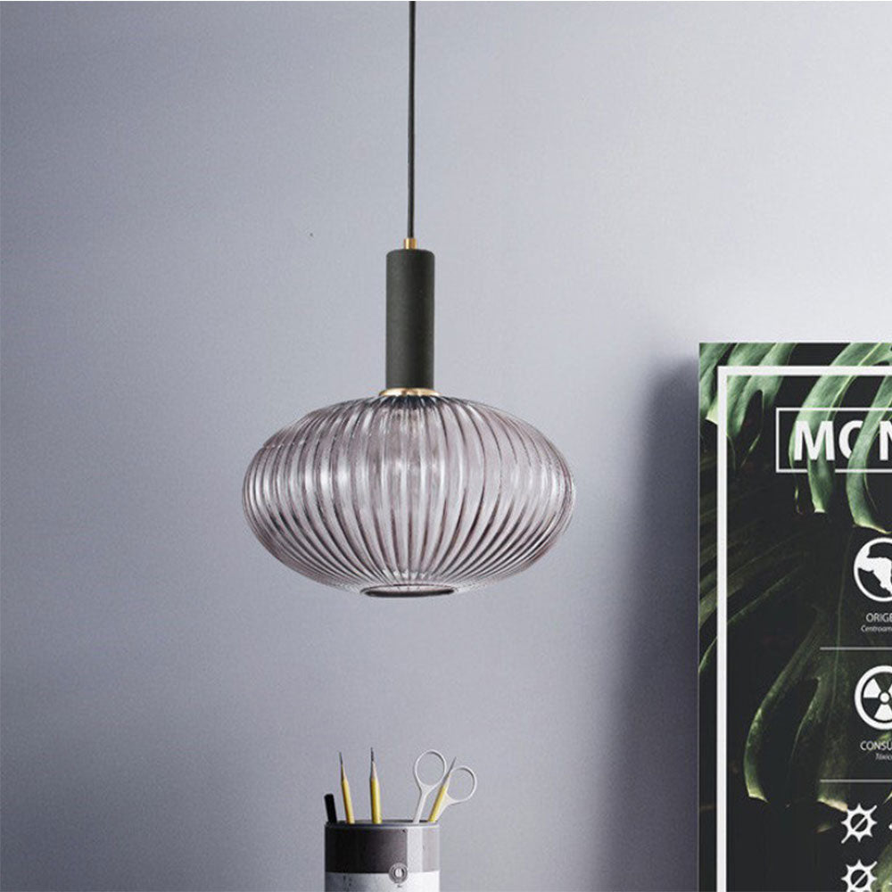 Smoke grey reeded glass pendant from Clérachic with a black fitting, hanging against a blue-grey wall beside a poster and a desk pot of pencils.