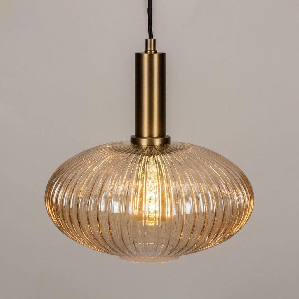 Close view of the amber reeded glass and brushed gold stem on this Clérachic pendant, with the bulb glowing inside the shade.