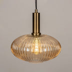 Close view of the amber reeded glass and brushed gold stem on this Clérachic pendant, with the bulb glowing inside the shade.