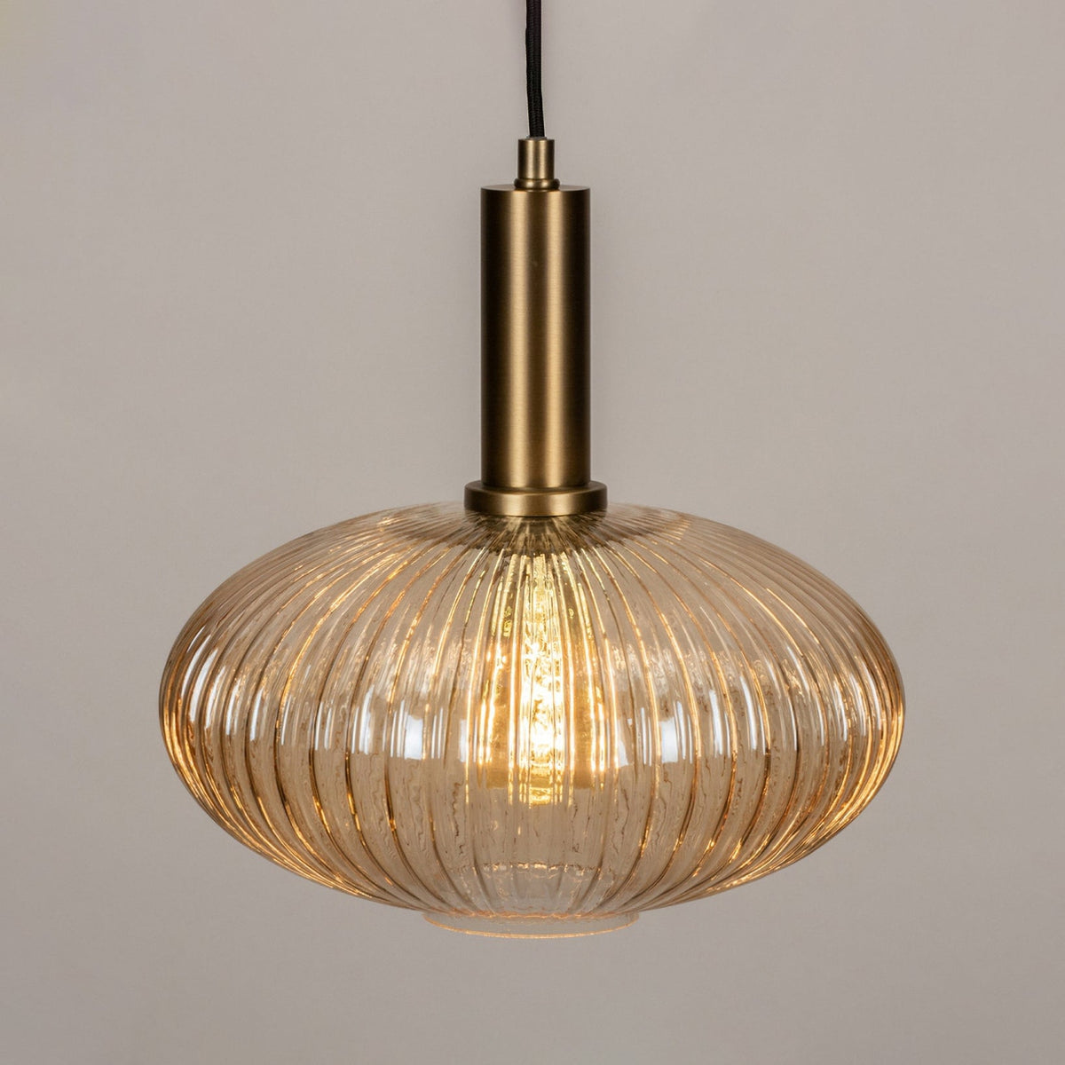 Close view of the amber reeded glass and brushed gold stem on this Clérachic pendant, with the bulb glowing inside the shade.