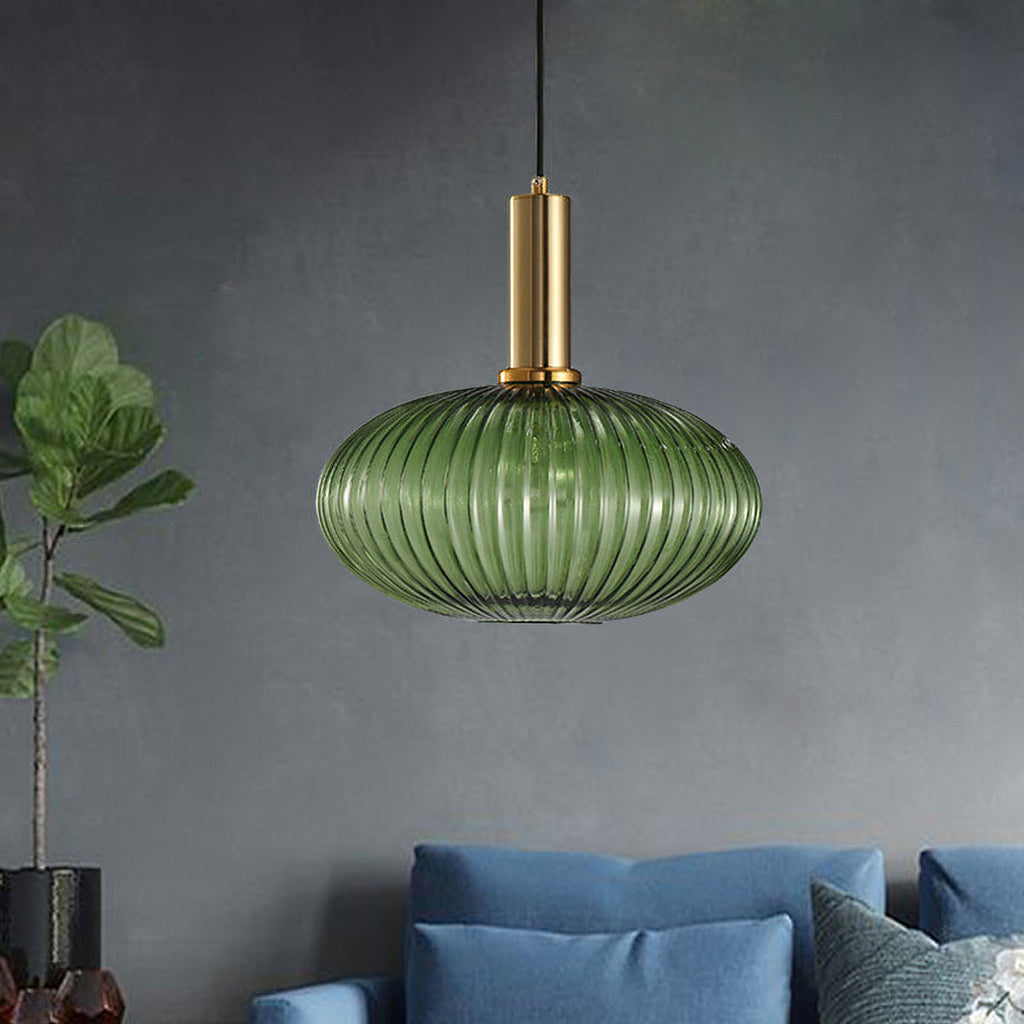 Flat green reeded glass pendant from Clérachic on a gold stem against a dark slate wall, with a blue sofa and a plant at the edge.