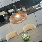 Lit amber reeded glass pendant from Clérachic hung low over a dark wooden table, with a modern kitchen and a glass bowl of apples behind.