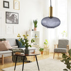 Flat smoke grey reeded glass shade from Clérachic on a gold stem, hung in a bright living room with a sofa, framed prints and plants.