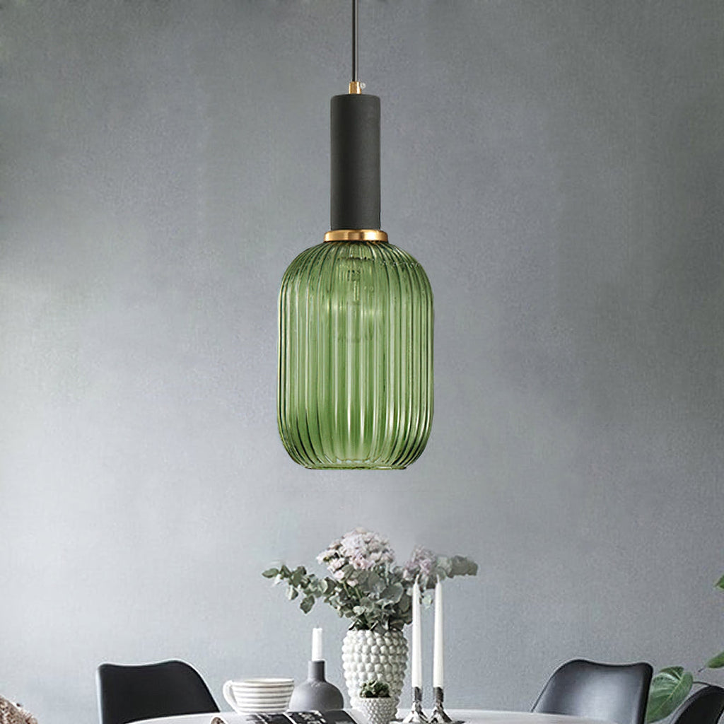 Green reeded glass pendant from Clérachic with a black fitting and gold ring, hanging against a grey wall above a laid dining table.
