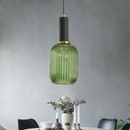 Green reeded glass pendant from Clérachic with a black fitting and gold ring, hanging against a grey wall above a laid dining table.