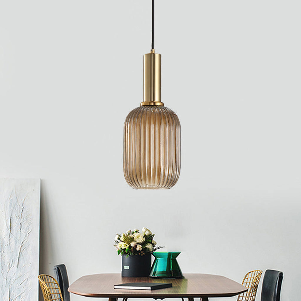Tall amber reeded glass pendant from Clérachic on a gold stem, hanging in a pale room with a small table set with flowers.