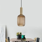 Tall amber reeded glass pendant from Clérachic on a gold stem, hanging in a pale room with a small table set with flowers.