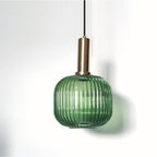 Round green reeded glass shade on a gold stem from Clérachic, close up against a white wall, with its shadow falling softly beside it.