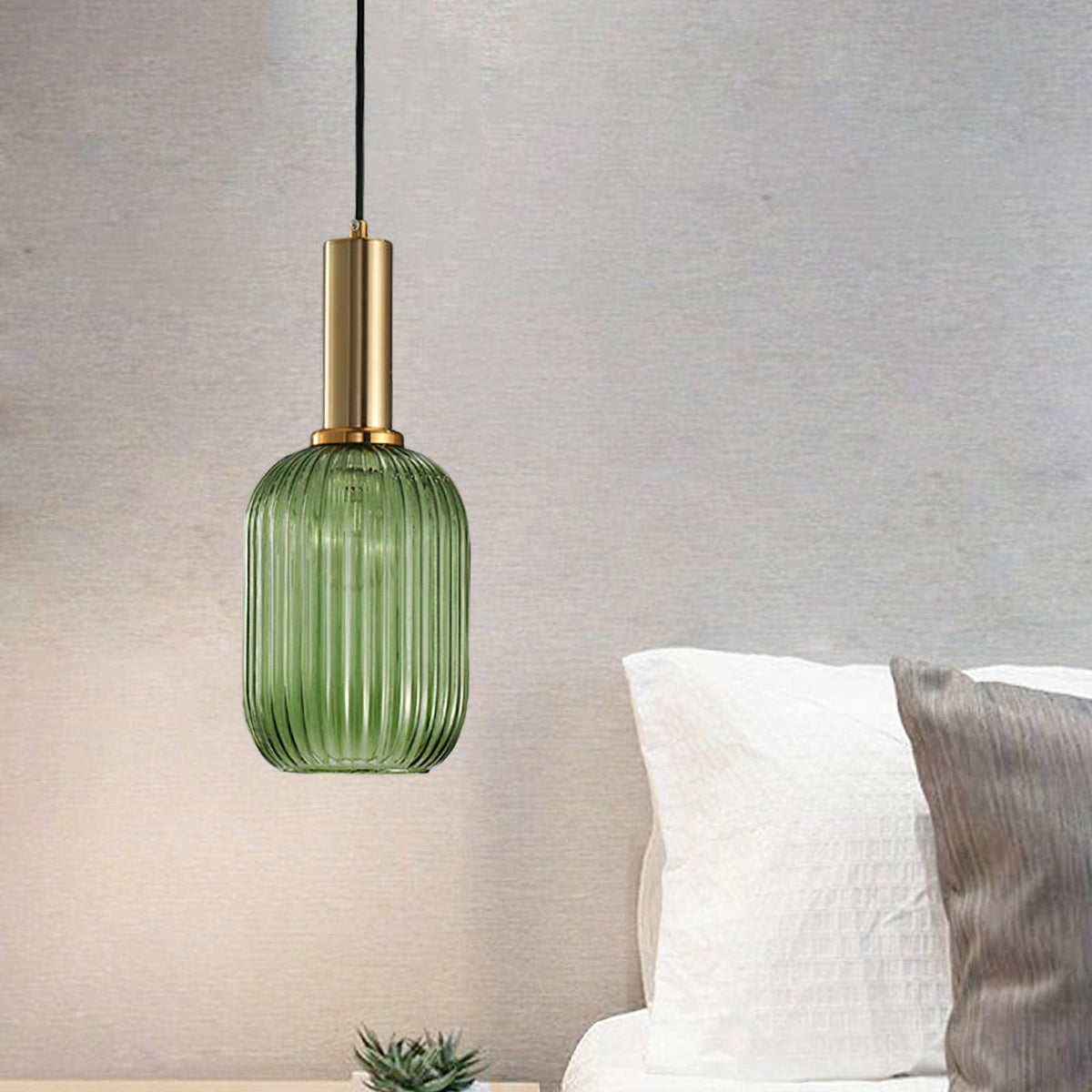 Tall green reeded glass pendant from Clérachic on a gold stem, hanging in front of a grey wall beside a white bed.