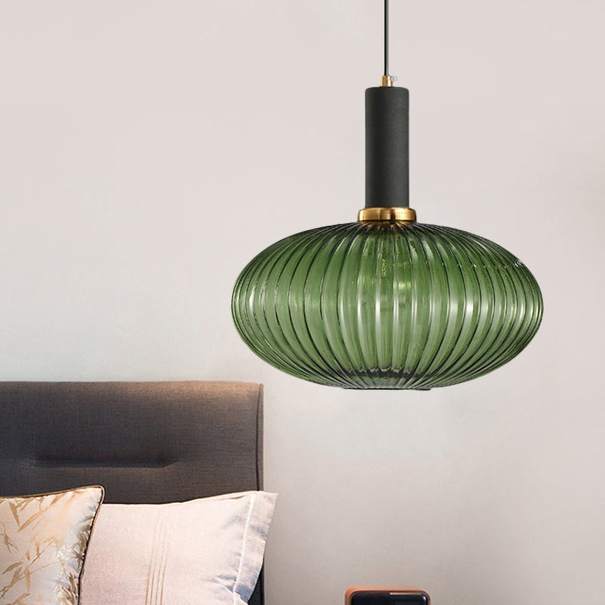 Flat green reeded glass pendant from Clérachic with a black fitting hangs above a bed with a grey headboard and cream cushions.