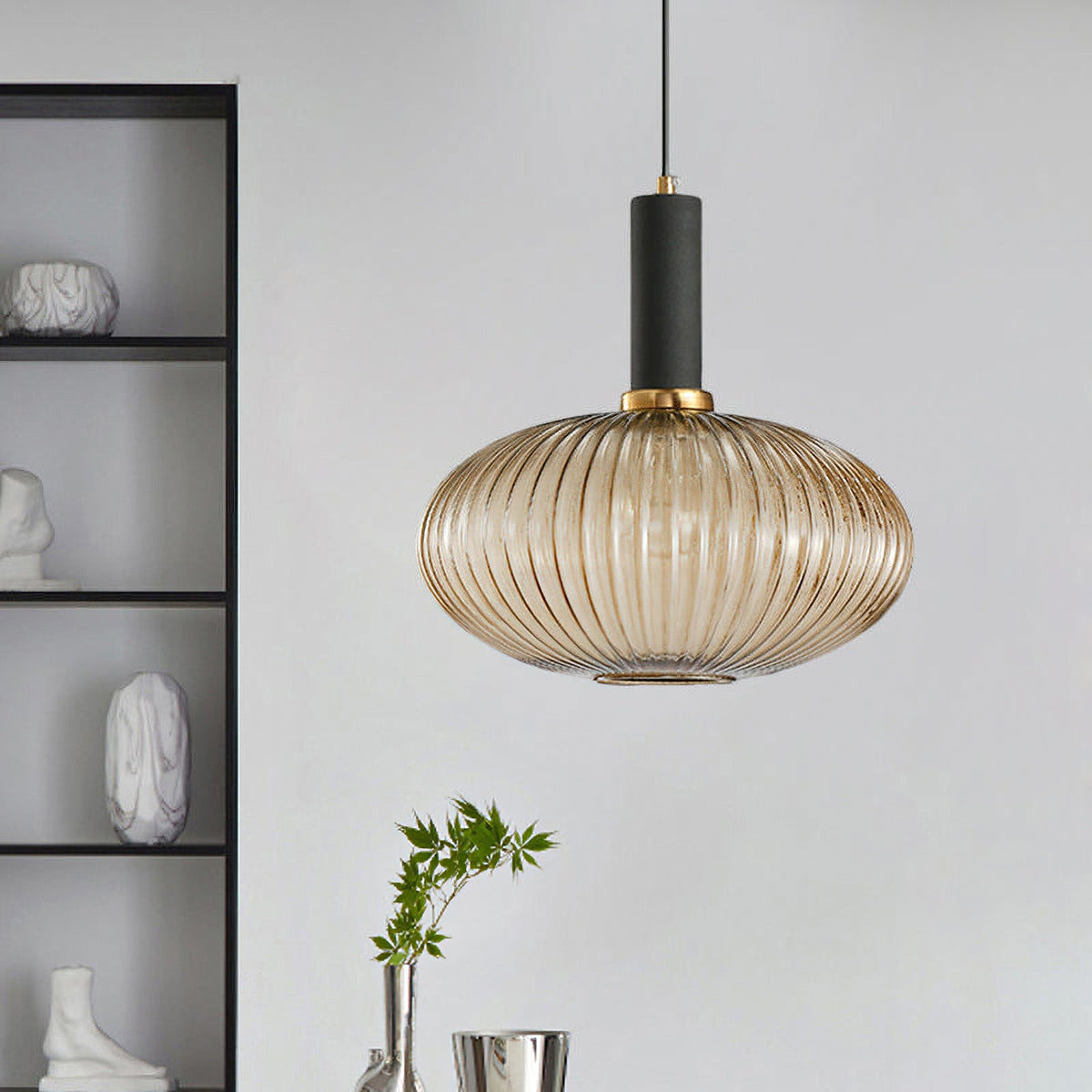 Amber reeded glass pendant from Clérachic with a black fitting hangs in front of a grey wall unit with ornaments on its shelves.