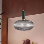Smoke grey reeded glass pendant from Clérachic with a black fitting hangs against a terracotta wall above a pink sideboard.