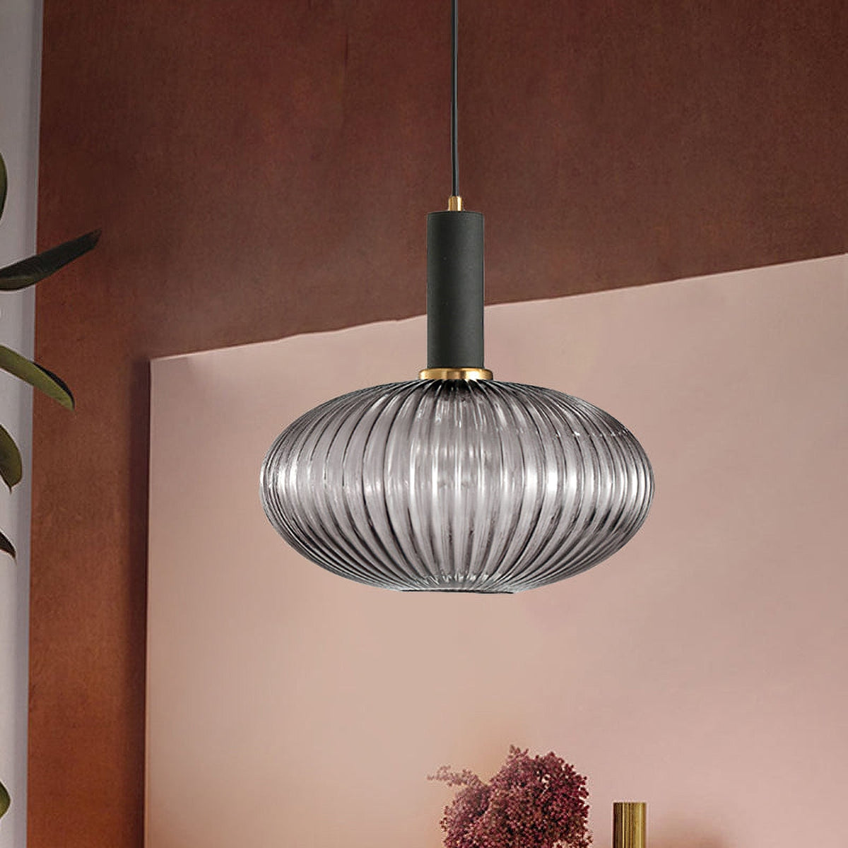 Smoke grey reeded glass pendant from Clérachic with a black fitting hangs against a terracotta wall above a pink sideboard.
