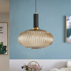Amber reeded glass pendant from Clérachic with a black fitting hangs against a blue wall near framed pictures and a basket of flowers.
