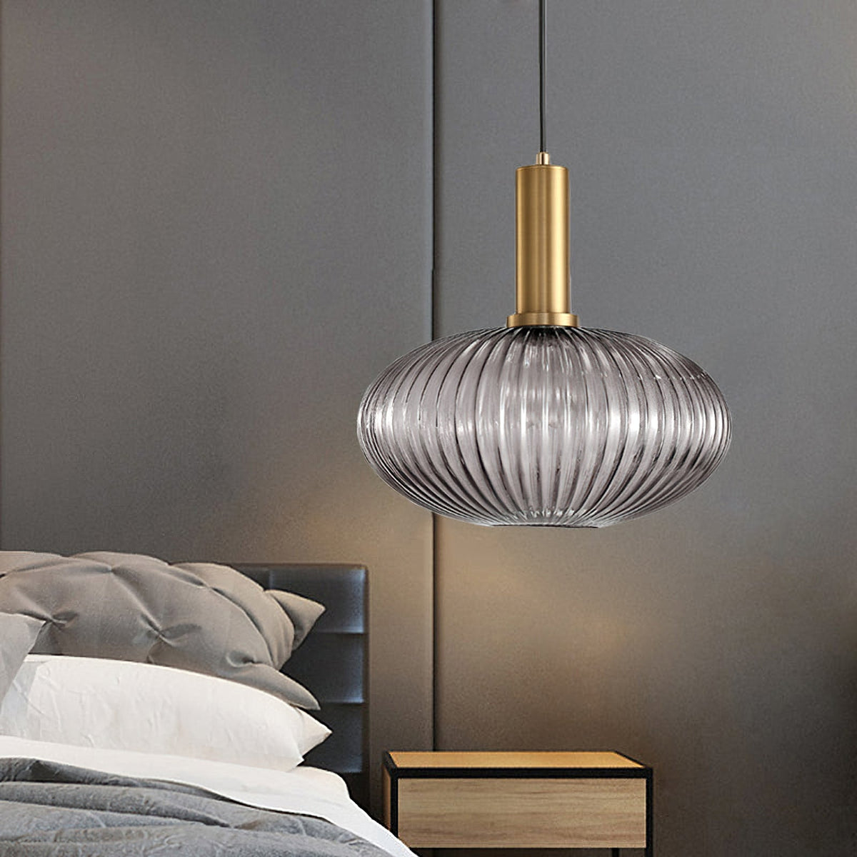 Smoke grey reeded glass pendant from Clérachic on a gold stem hangs beside a bed, with a wooden bedside table and a grey headboard.