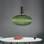 A wide green reeded glass pendant from Clérachic with a black fitting hangs above a white round table with a pink cushion.