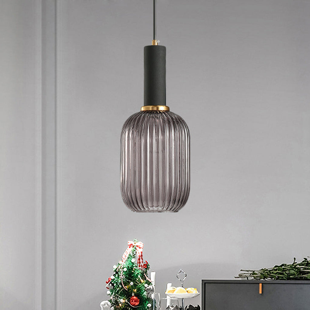 Tall smoke grey reeded glass pendant from Clérachic with a black fitting, hanging against a grey wall beside a dark sideboard and a Christmas tree.