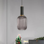 Tall smoke grey reeded glass pendant from Clérachic with a black fitting, hanging against a grey wall beside a dark sideboard and a Christmas tree.