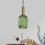 Small tall green reeded glass pendant from Clérachic on a gold stem, hanging above a table laid with wine glasses, a carafe and candles.