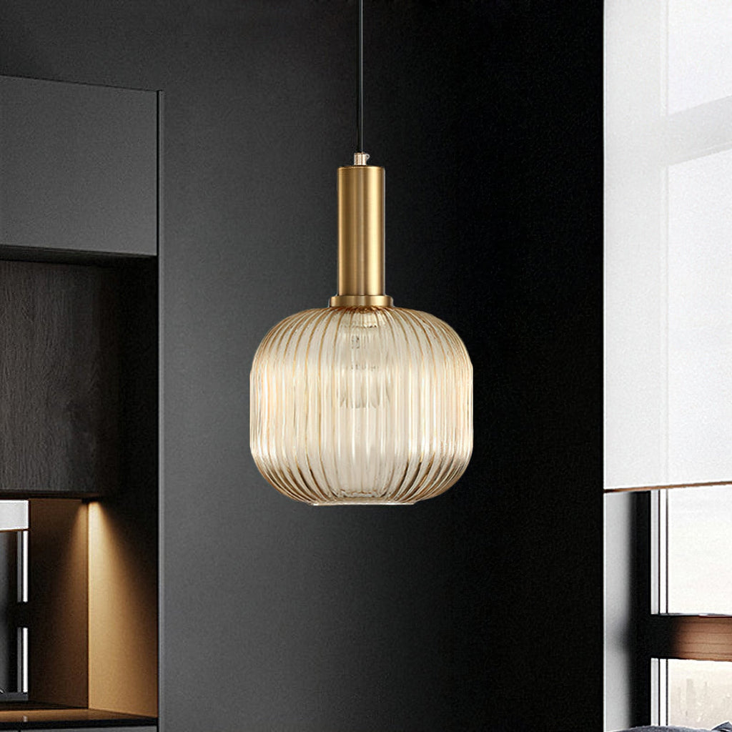 A round amber reeded glass pendant from Clérachic on a gold stem hangs against a dark kitchen unit, glowing softly.