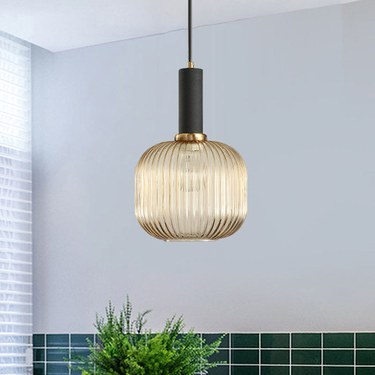 Rounded amber reeded glass pendant from Clérachic with a black fitting, hung against a blue-grey wall with a green tiled counter below.