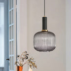 Rounded smoke grey reeded glass pendant from Clérachic with a black fitting hangs by a white-framed window with dried berry stems below.