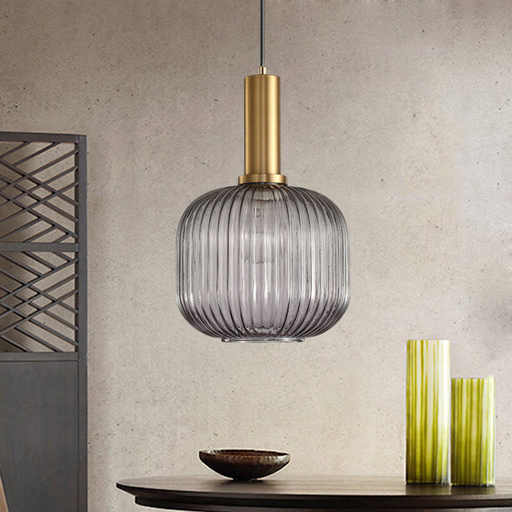 Rounded smoke grey reeded glass pendant from Clérachic on a gold stem hangs against a stone-effect wall, with green vases and a dark bowl.