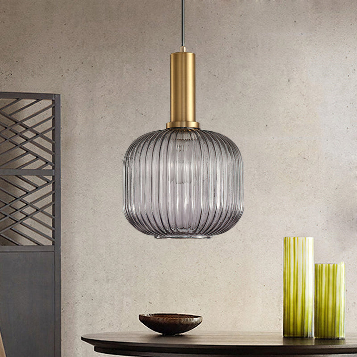 Rounded smoke grey reeded glass pendant from Clérachic on a gold stem hangs against a stone-effect wall, with green vases and a dark bowl.